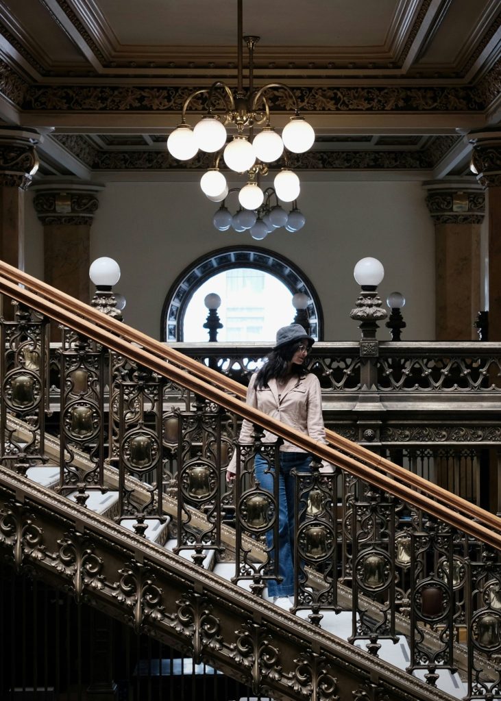Woman walking down ornate staircase with chandelier